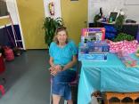 Photo of one of our vendors sitting next to her booth table displaying miscellaneous household items and collectables for sale.